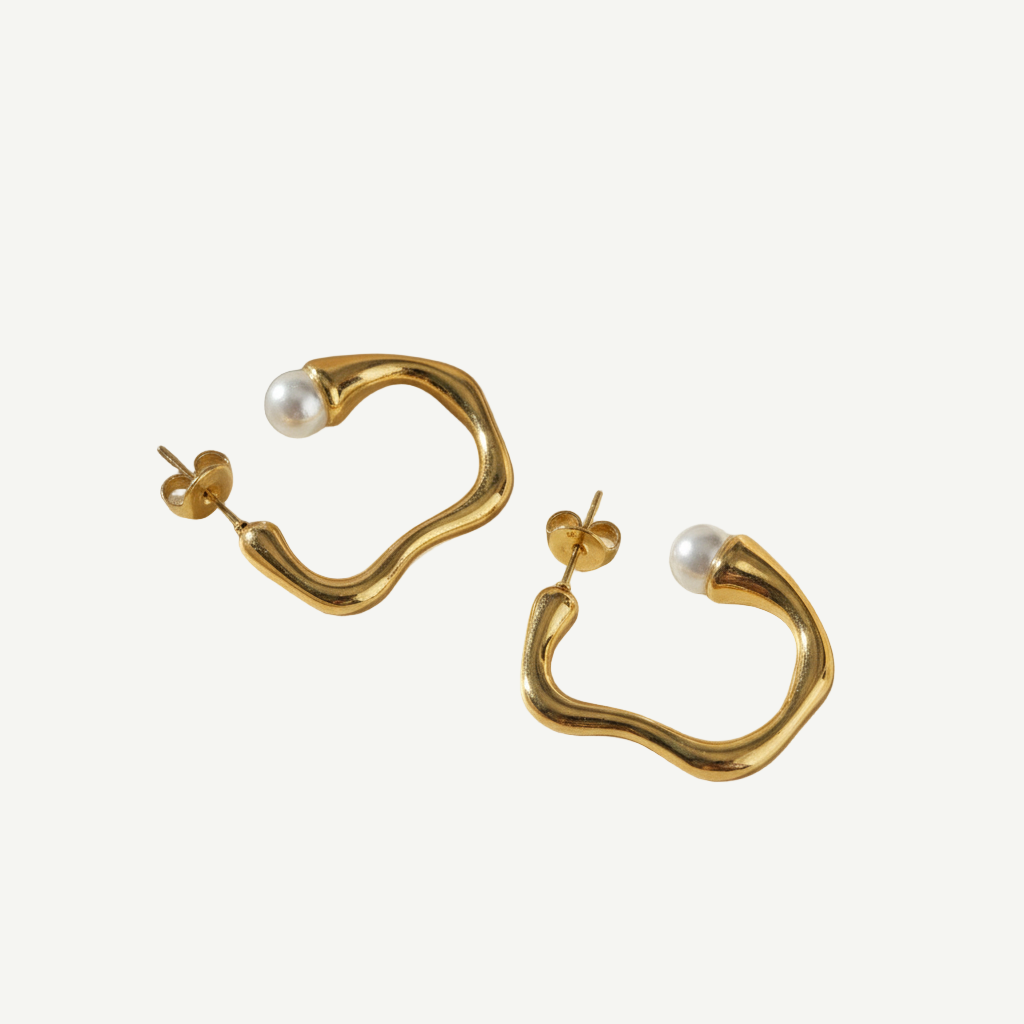 Pendientes Aura Pearl Curve en latón con baño de oro y detalle de perlita. Ligeros, elegantes y minimalistas, perfectos para looks diarios o sofisticados.
